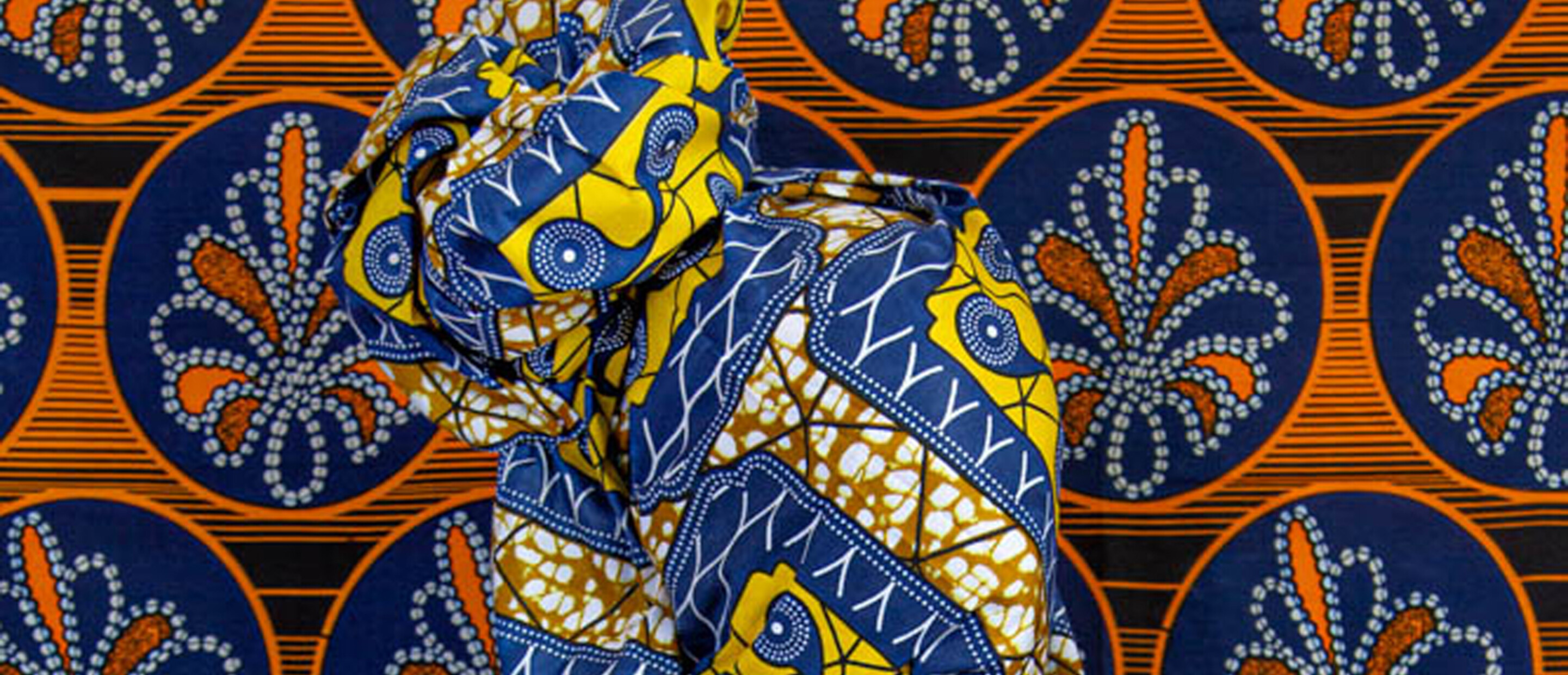 Photograph of figure draped in patterned fabric with patterned fabric as background