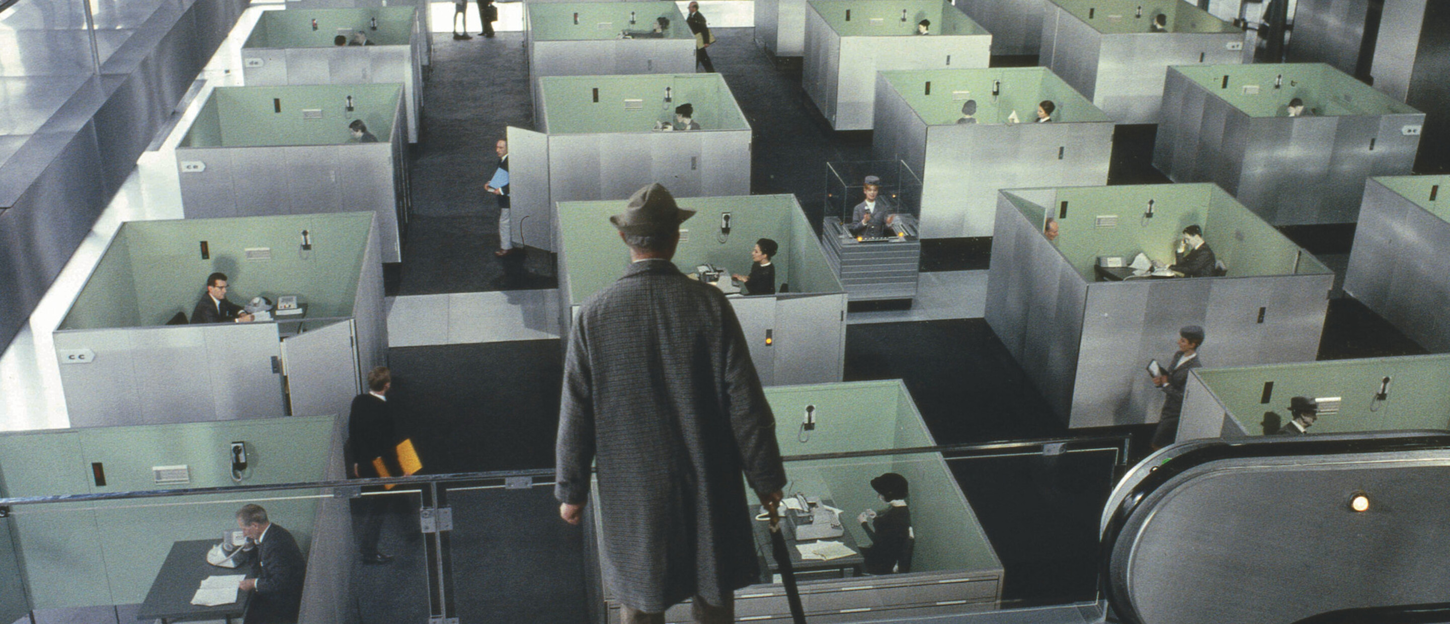 man in top hat and long coat looking down at rows of cubicles