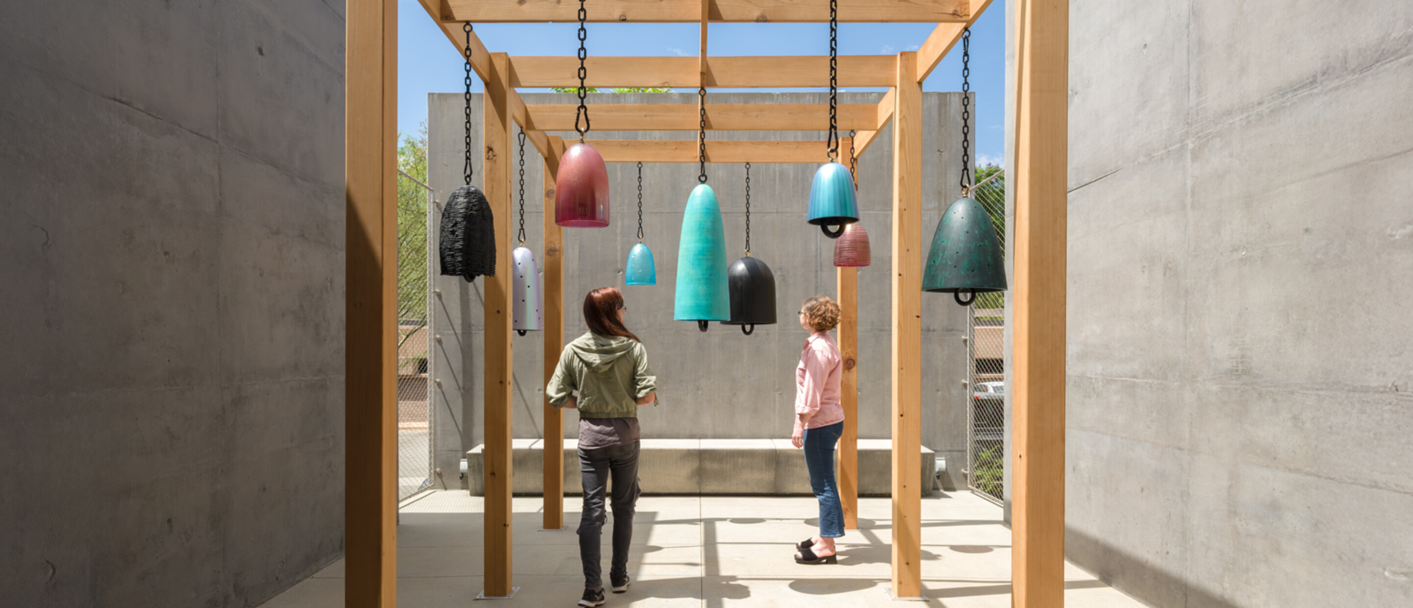two people stand under glass and bronze bells in outdoor patio