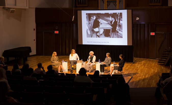 Panel of 5 people in front of a projection screen with an auditorium filled with audience members