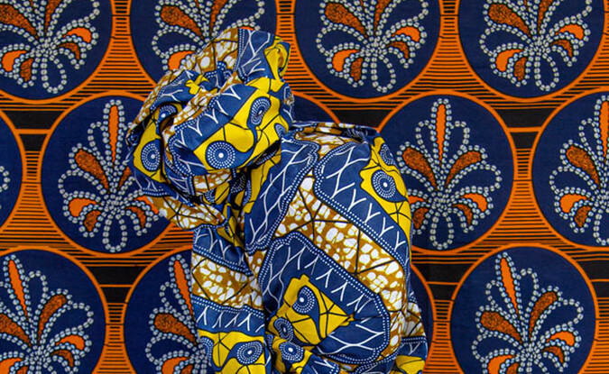 Photograph of figure draped in patterned fabric with patterned fabric as background