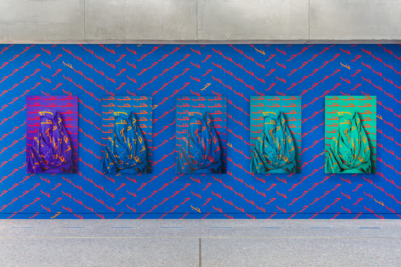 Installation view of Alia Ali's site-specific installation of Love with 5 photographs on blue wall with patterns of Love painted in Arabic