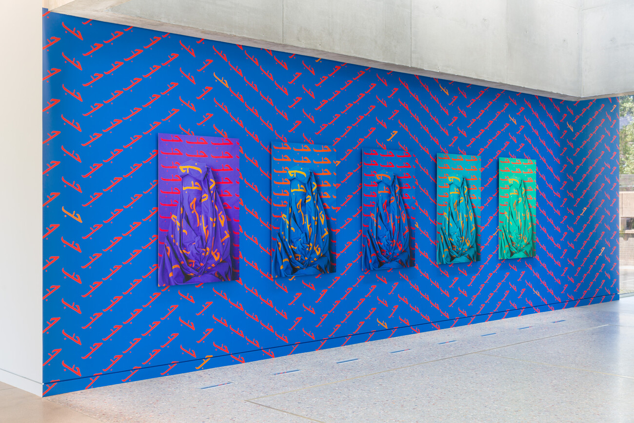 Installation view of Alia Ali's site-specific installation of Love with 5 photographs on blue wall with patterns of Love painted in Arabic