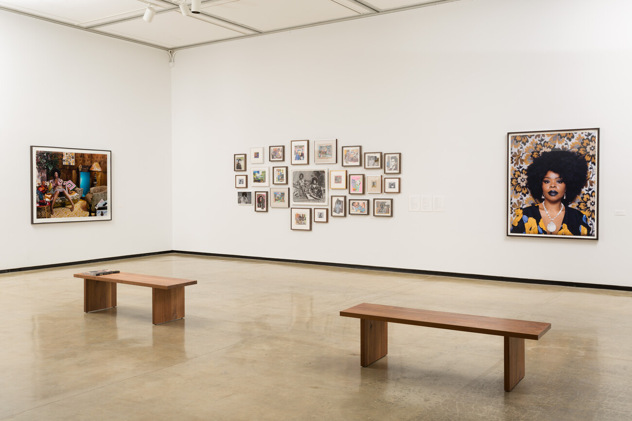 Installation view of a gallery with photographs and montage of 2-dimensional works with 2 wooden benches on the floor