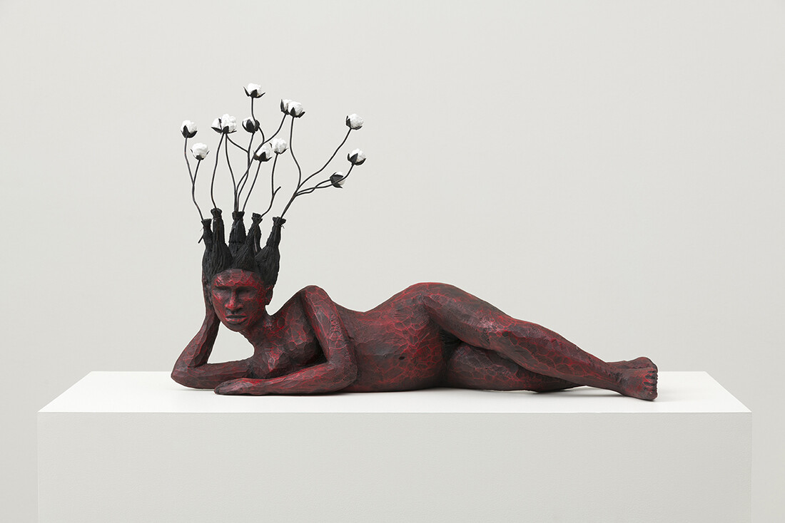 Red body sculpture laying down with flowers moving upwards