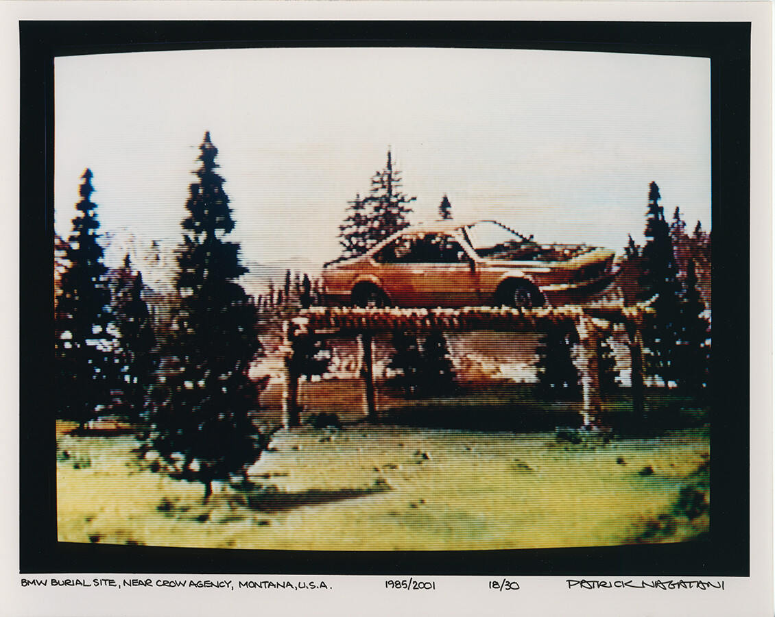 Photo of TV screen showing trees with brown car hoisted on pedestal