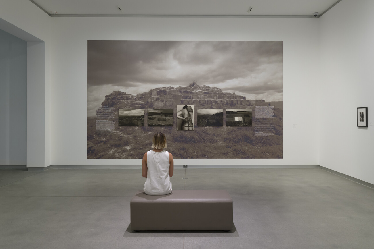 woman sits on bench in gallery in front of larger gray photograph on the wall
