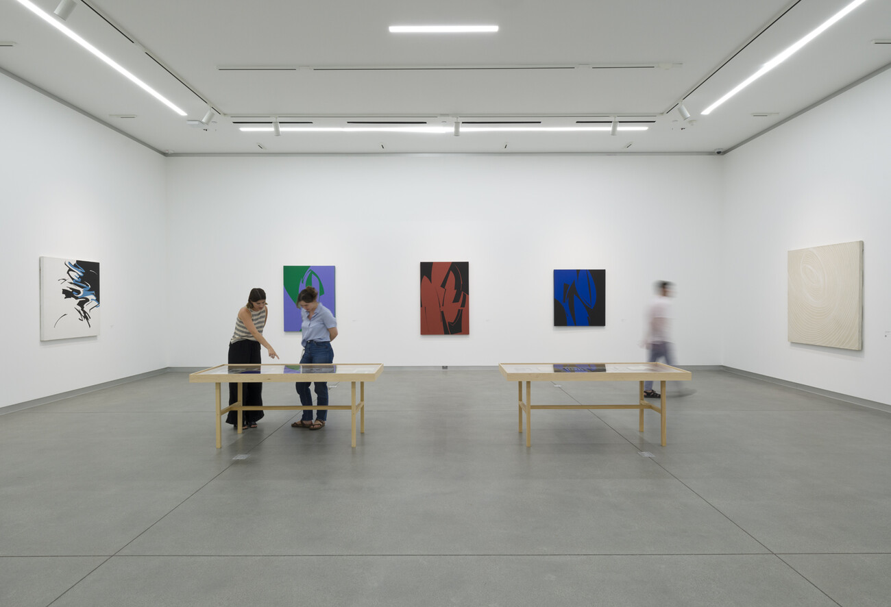gallery with three people looking at art on tables and walls