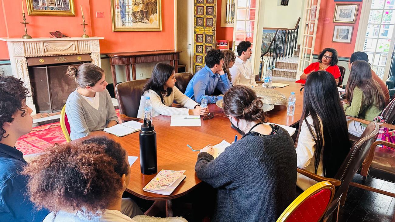 students sitting around a table listening to a speaker