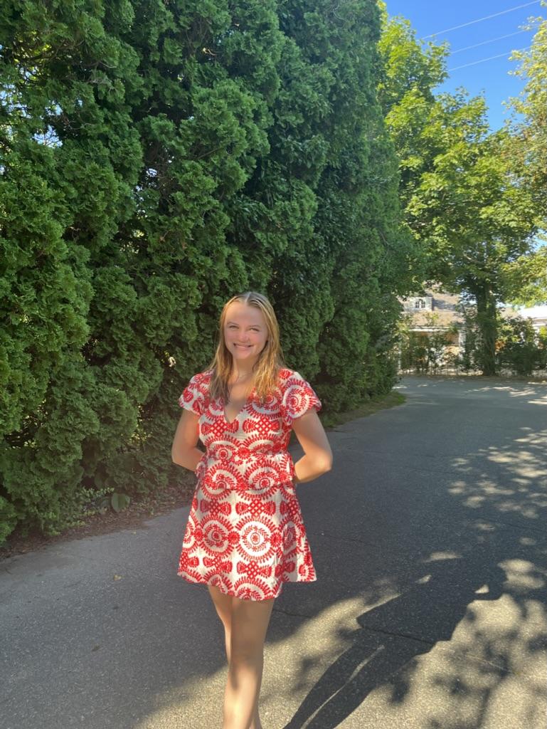 Student poses in front of line of tall bushes 