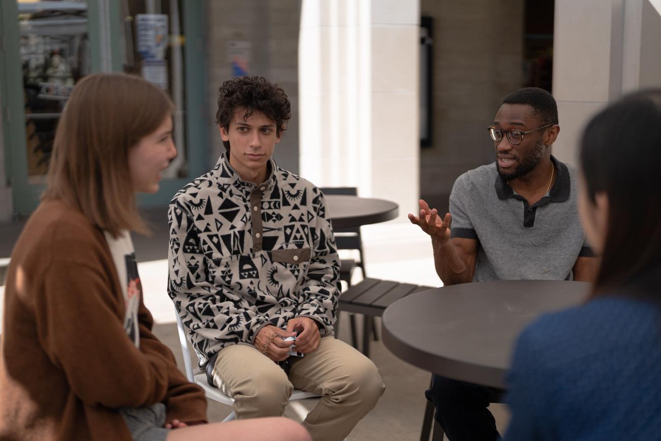 Four students sit around an outdoor table discussing something