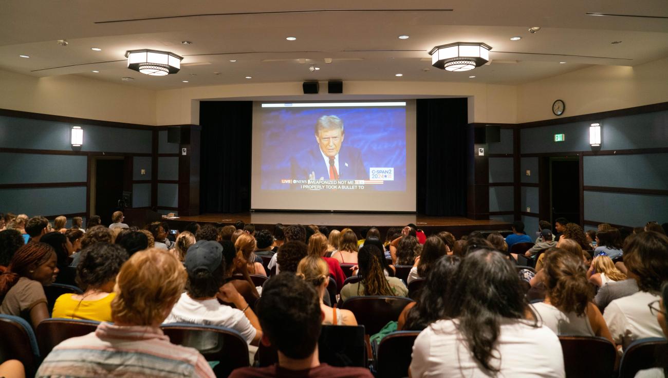 Students sit in an auditorium watching a big screen