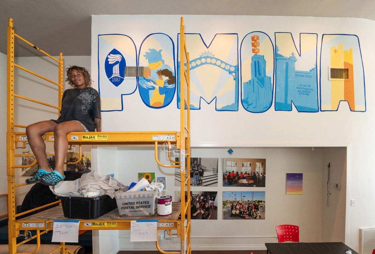 Student sits on platform in front of mural on wall. 