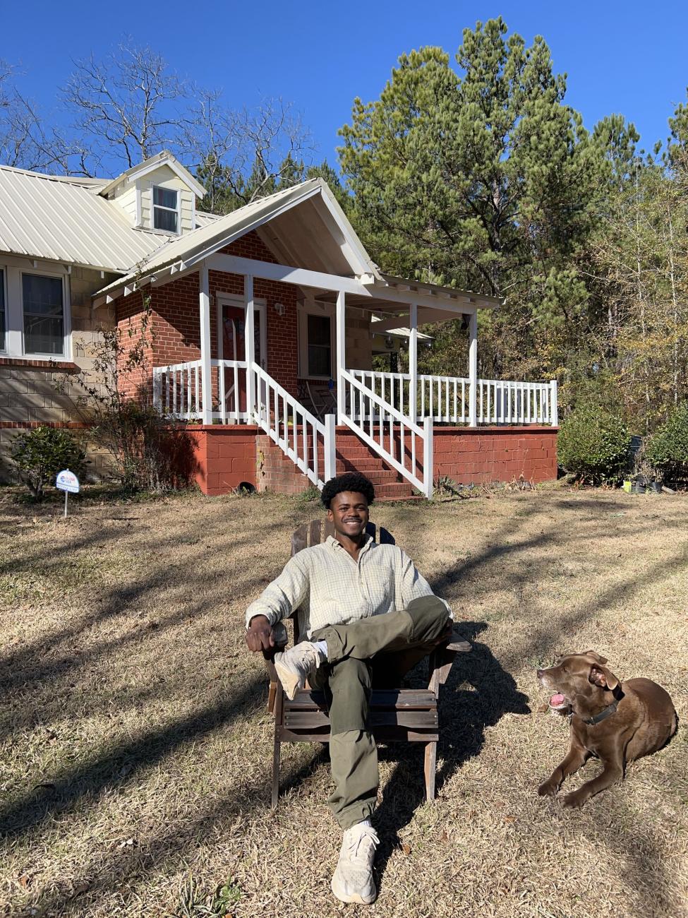 Ivan Soloman sits on a chair outside with his dog on the ground next to him.