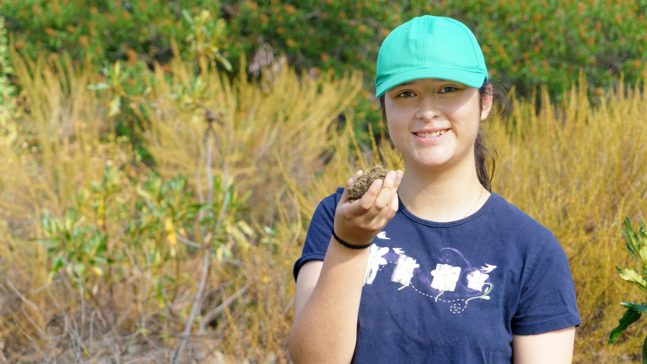 Photo of student in a field holding research specimen.