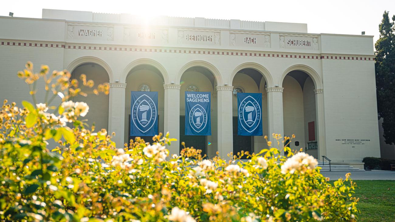 White building called Bridges Auditorium has three banner flags.